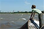 Boy standing on graffitied metal, looking at polluted bay