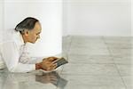 Senior man lying on tiled floor reading book