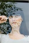 Young woman with eyes closed, drawing pair of glasses on window