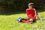 Teenage Boy Wearing Soccer Uniform and Sitting on Grass