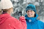 Femme prenant la photo de l'homme avec le téléphone appareil photo à l'extérieur en hiver, Whistler, Colombie-Britannique, Canada