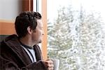 Man in Bathrobe Holding a Cup of Coffee and Gazing Out the Window