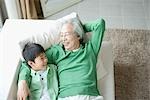 Senior man with grandson relaxing on couch