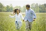 Mature man and a mid adult woman holding hands and running in a field