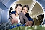 Young couple taking clothes out of dryer at Laundromat smiling
