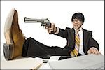 Businessman sitting at desk pointing shotgun at foot