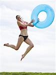 Woman in bikini jumping and smiling with swimming ring