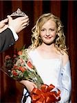 Girl holding red roses being crowned with tiara smiling