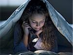 Girl laying in bed under blanket with flashlight reading