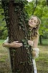Frau umarmt Baum mit Augen geschlossen