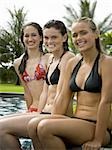 Portrait de trois jeunes filles souriantes et assis au bord de la piscine