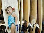 Portrait of a baby girl leaning against a surfboard