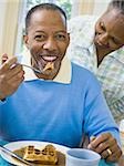 Close-up of a senior man having breakfast with a senior woman behind him