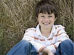 Portrait of a boy sitting against a hay bale