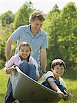 man pushing his son and daughter in a wheelbarrow