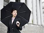 Portrait of a female lawyer standing on the steps of a courthouse and holding an umbrella