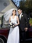 Portrait of a newlywed couple standing near a car in front of a chapel