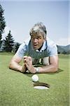 Close-up of a man kneeling in front of a golf ball near a hole and praying