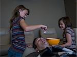 Daughters dropping popcorn into sleeping father's mouth