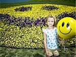 Girl on a hill holding happy face balloon