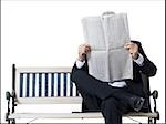 Businessman sitting on bench reading newspaper