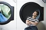 Homme assis dans la laverie automatique avec bras croisés regarder sécheuse