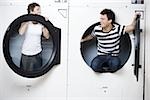 Man and woman in Laundromat dryers smiling