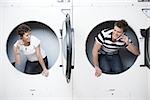 Two people in dryers at Laundromat with cell phones