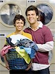 Paar mit Kleidung in den Wäschekorb im Waschsalon lächelnd