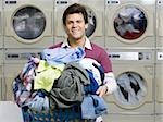 Man with clothing in laundry basket at Laundromat smiling