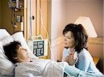 Woman holding hands with mature woman in hospital bed