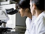 Weibliche Lab Technician Blick durchs Mikroskop mit männlichen Techniker