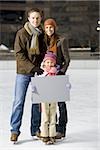 Man and woman with girl holding blank sign outdoors in winter