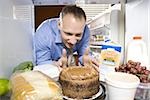 Man in refrigerator dipping finger in chocolate cake