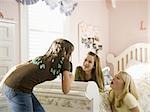 Girl singing into hairbrush in bedroom with girlfriends laughing
