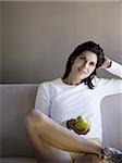 Woman sitting on sofa with green apple