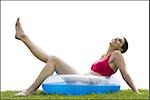 Woman sitting in swimming ring on grass with leg up smiling