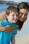 Woman embracing boy wrapped in towel outdoors smiling