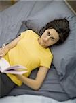 Frau im Bett mit Notizbuch und Stift lächelnd