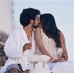 Couple sitting outdoors with champagne flutes and scenic background smiling and snuggling