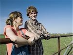 Brother and sister leaning on wooden fence in field with blue skies