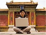 Businesswoman sitting cross legged outdoors with laptop