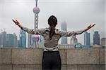 Businesswoman outdoors with arms up and city skyline in background rear view