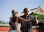 Mature couple dancing outdoors with blue sky and pagoda in background