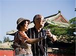 Mature couple dancing outdoors with blue sky and pagoda in background