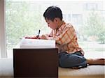 Boy sitting with workbook in front of large window