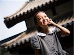Jeune fille debout à l'extérieur avec le téléphone cellulaire en face de la pagode souriant