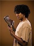 young man in a brown shirt holding a shoe and his nose.