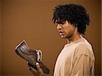 young man in a brown shirt holding a shoe and his nose.