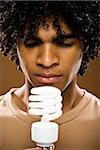 young man in a brown shirt holding light bulbs.